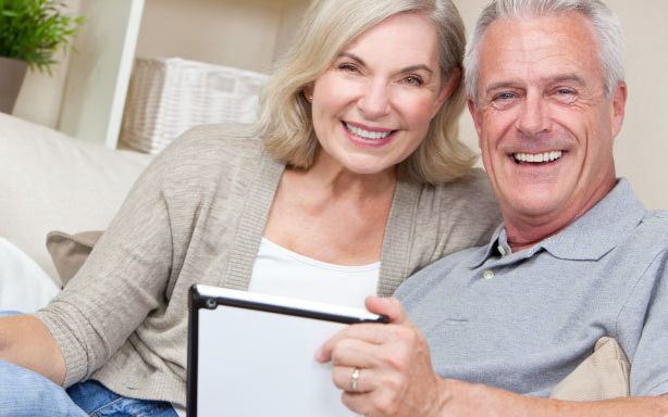 Older couple smiling at the camera over an iPad