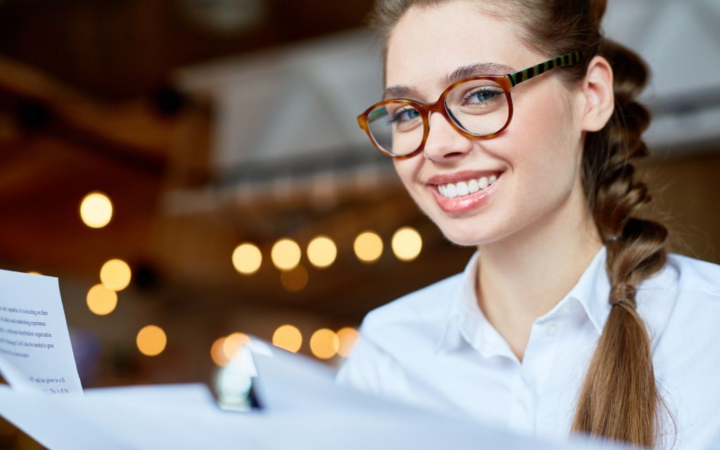 Brunette woman in glasses smiling at the camera over paperwork